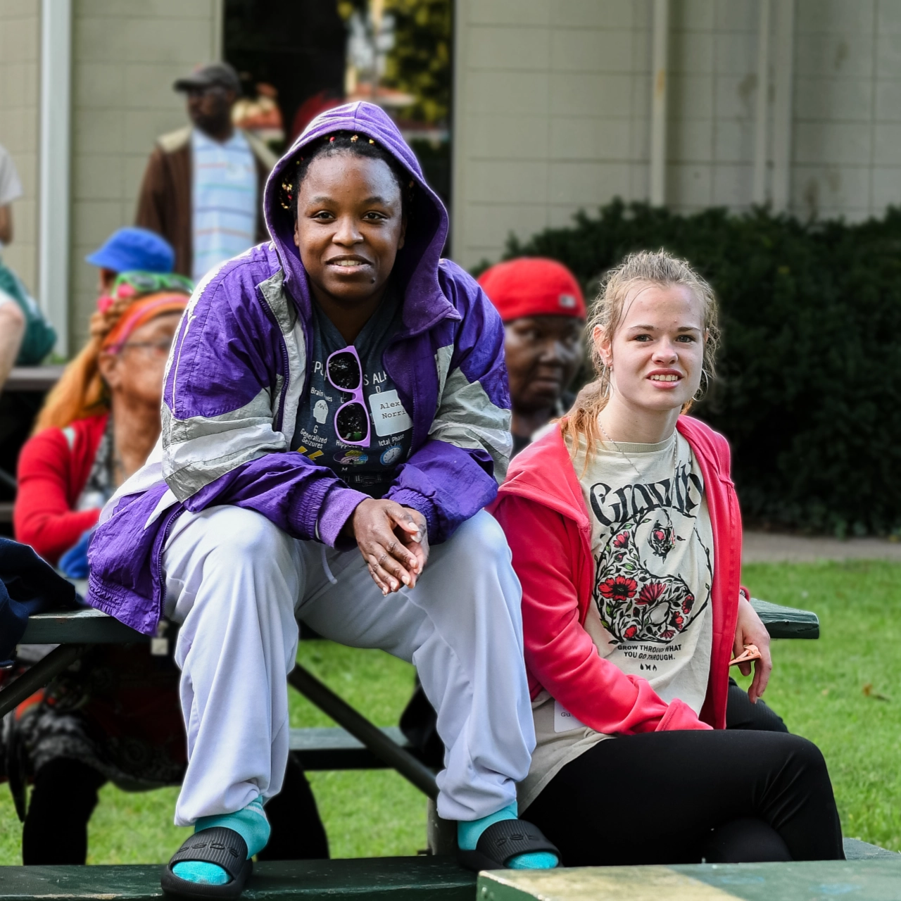 Two River Valley Special Rec participants smile together while sitting outside on a picnic bench on a spring day.